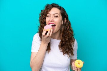 Young caucasian woman isolated on blue background eating a donut