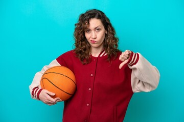 Young caucasian basketball player woman isolated on blue background showing thumb down with...