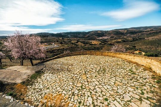 Landscape of a circular, cobblestone threshing floor where cereals were threshed and then winnowed for grain with almond trees in bloom and rural scenery