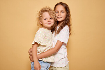 Little girl showing her affection for her baby sister with warm embrace reflecting strong sibling bond and happiness of childhood isolated over beige background