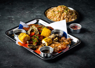 Filipino Feast with Grilled Meat, Garlic Fried Rice, Grill corn cob, Boneless Chicken Slice, Beef Belly Brisket, Pork Belly and Sauces served in tray side view of international platter