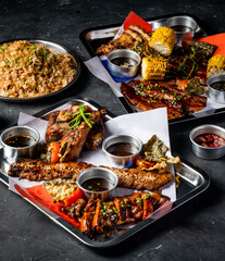 Filipino Feast with Grilled Meat, Garlic Fried Rice, grill corn cob, Peri Peri Chicken, Jerk Chicken, Beef Belly Brisket, Pork belly, tomato, and Sauces served in tray side view of platter