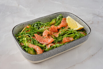 Fresh salad with smoked salmon, arugula, cucumbers, and lemon wedge served on a plate