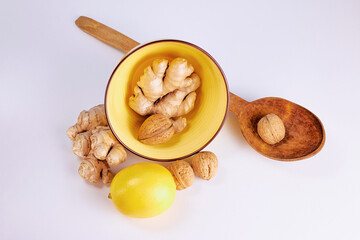 ginger in a yellow deep plate, nut in a large wooden spoon and lemon on a light background, top view
