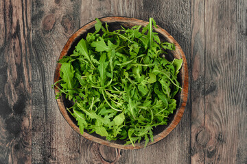Fresh green arugula leaves served in a rustic wooden bowl on a textured wooden table
