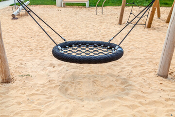 A swing in the shape of a bird's nest on a sand-covered playground. Entertainment complex for...