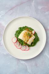 Elegant white cod fish served on vibrant spinach puree with sliced radishes, garnished for visual appeal