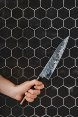 A close-up of a hand gripping a sharp kitchen knife against a hexagonal tile background