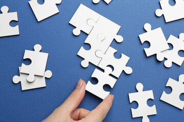 Fototapeta premium Woman solving white puzzle on blue background, top view