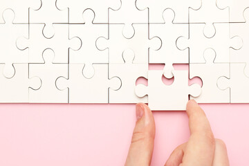 Woman solving white puzzle on pink background, closeup