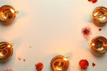 Diwali celebration. Diya lamps and beautiful flowers on light textured surface, flat lay. Space for text