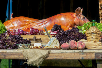 A roasted suckling pig placed among vegetables, fruits, cheese, and nuts. © photoPepp