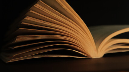 open book on black background. a little light shining on a part of an old open book on a dark background