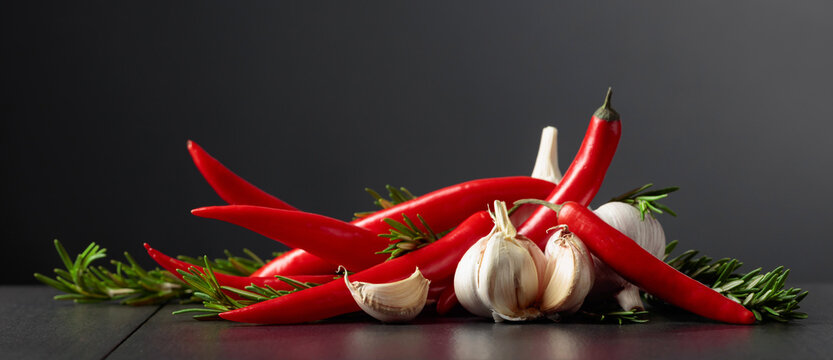 Red hot chili peppers, garlic, and rosemary on a black background.