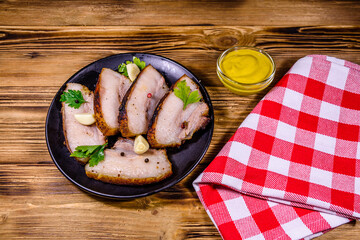 Slices of baked pork belly, garlic and parsley on a black plate