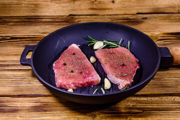 Raw steaks with garlic, rosemary and spices in a cast iron grill pan