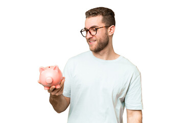 Young man holding a piggybank over isolated chroma key background with happy expression