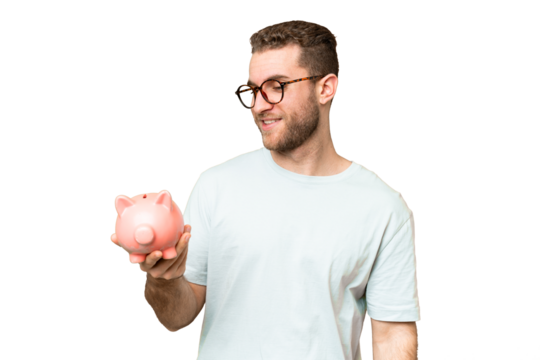 Young man holding a piggybank over isolated chroma key background with happy expression