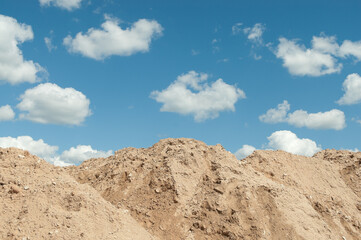 a mountain of sand against a blue sky and clouds