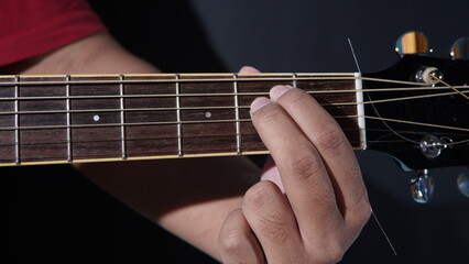 the hand of a person playing an acoustic guitar with his fingers forming the E minor chord. E minor...