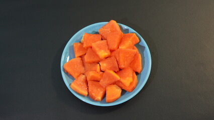 papaya slices on a blue plate on a black background