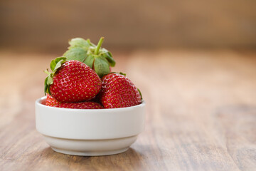 Fresh strawberries in white bowl on wood background with copy space