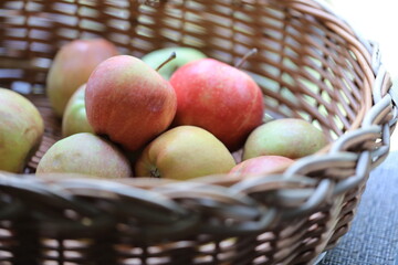 A basket filled with fresh apples sits atop a wooden table, perfect for snacking or decorating.