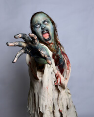 Close up portrait of scary female model wearing spooky halloween costume, ripped apocalyptic clothes, dropping fake blood like an undead zombie character. Isolated figure on studio background