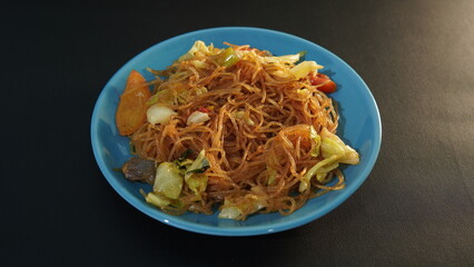 Fried vermicelli ( bihun goreng ) on a blue plate on a black background