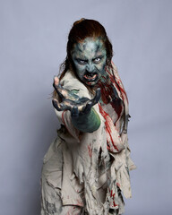 Close up portrait of scary female model wearing spooky halloween costume, ripped apocalyptic clothes, dropping fake blood like an undead zombie character. Isolated figure on studio background