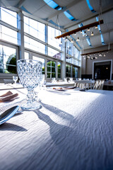 Crystal glass on the table in a bright, glass-walled banquet hall. Photo taken during the day, with sunlight streaming in.