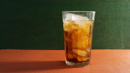 A glass of iced tea on a wooden table with a green wooden plank in the background