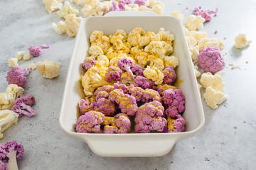 Cauliflower, white and purple, in baking pan with garlic seasoning, ready to be baked.