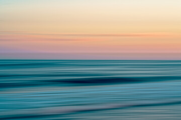 Blurred ocean waves meet a pastel sky at sunset.