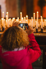 A girl takes pictures on her phone of the altar and candles in the church. Faith, light, religion,...
