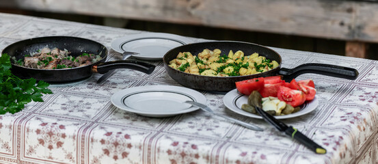 Two frying pans with cooked meat and potatoes, garnished with fresh herbs, placed on patterned...