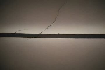 Fototapeta premium A close-up view of a wall with a prominent crack running horizontally across it, casting a shadow. The background is a muted tone, emphasizing the texture and imperfections of the wall surface.