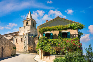 Charming narrow street in Venasque with sunlit stone and vibrant flowers, Provence, France. Narrow...