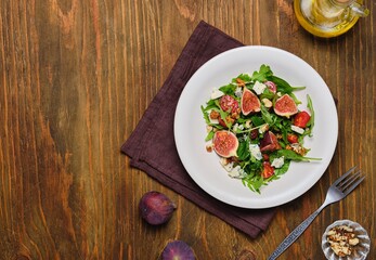Healthy salad with fresh figs, arugula, blue cheese and walnuts in a light ceramic plate on a wooden background. Recipes figs.