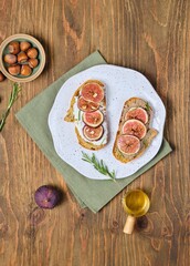 Two open sandwiches with fresh figs, ricotta and pate on a light ceramic plate on a wooden background. Recipes figs.