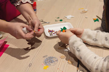 Children's hands make Christmas paper crafts under the guidance of a mentor