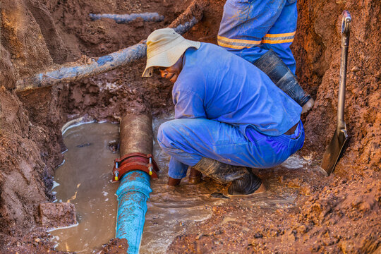 african american construction workers doing some trench digging, metal pipe repairing , water in the trench hole