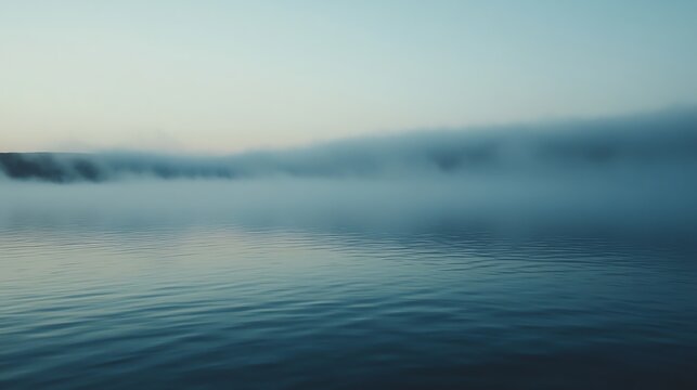 A body of water with fog rolling in over the trees in the distance.