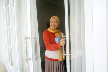 Young Asian Woman Holds Cup Of Coffee And Opening Door At Balcony