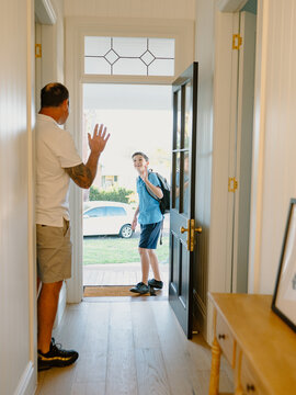 Young boy waving his hand goodbye to his dad at the doorway.