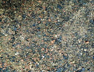 Multicolored asphalt texture with mixed stone granules, featuring earthy tones of brown, red, and black. Ideal for backgrounds, urban design, and construction projects.