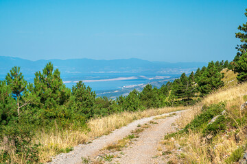 Unpaved road under blue sky through the hilly landscape of the Croatian Mountains.