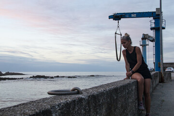 Blonde woman in black dress and barefoot sneakers knocking down a port crane