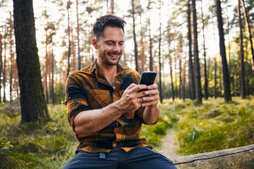 Happy man in forest using mobile phone during weekend hike