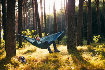 Happy man relaxing in hammock in forest during sunny autumn day